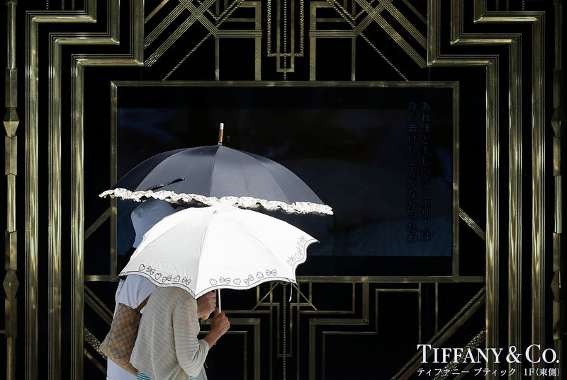 © Reuters. FILE PHOTO: Passers-by holding parasols walk in front of an advertisement for Tiffany & Co. at the Ginza shopping district in Tokyo