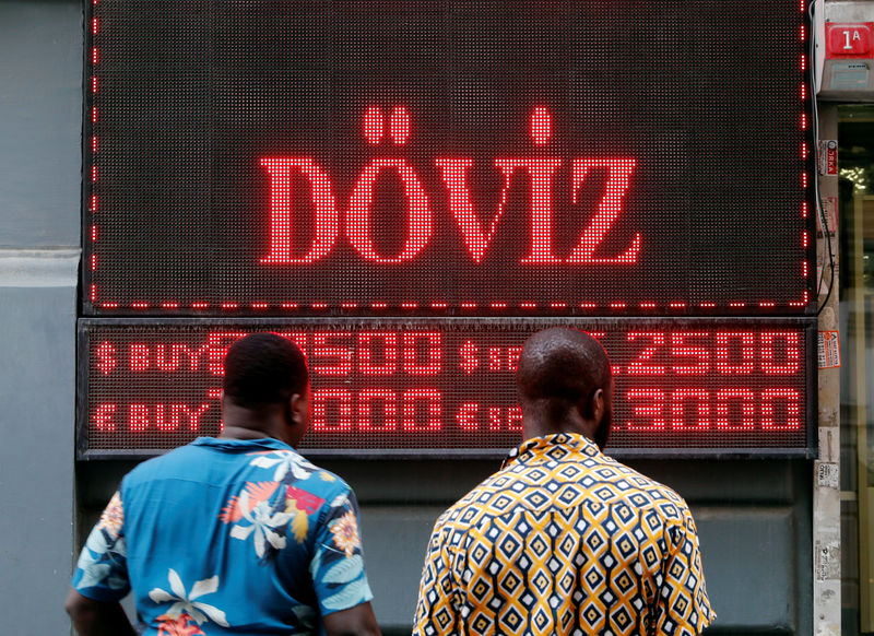 © Reuters. People look to a display board of a currency exchange office in Istanbul