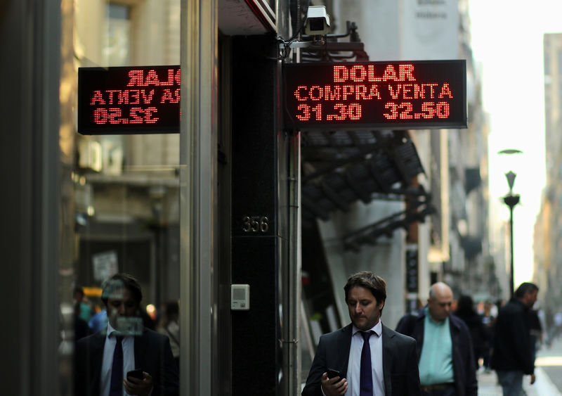 © Reuters. People walk past an electronic board showing currency exchange rates in Buenos Aires' financial district,