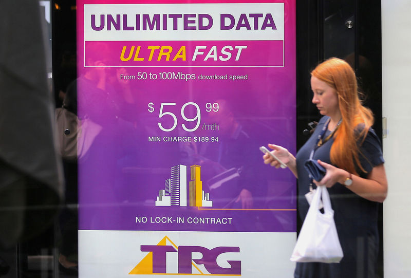 © Reuters. FILE PHOTO: A woman looks at her phone as she walks past an advertisement for Australia's TPG Telecom Ltd in central Sydney, Australia