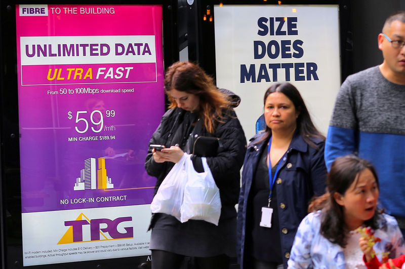 © Reuters. FILE PHOTO: A woman looks at her phone as she walks past an advertisement for Australia's TPG Telecom Ltd in central Sydney, Australia