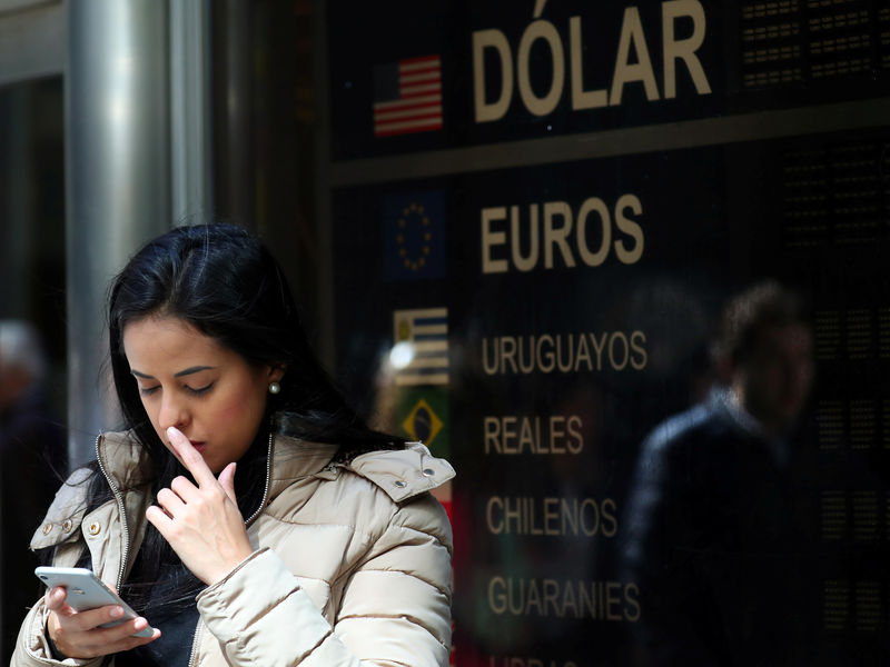 © Reuters. A woman looks at her cellphone as she stands in front of a currency exchange board in Buenos Aires' financial district