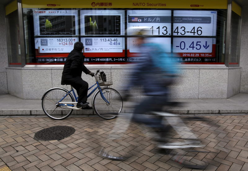 © Reuters. FILE PHOTO:  A man riding on a bicycle looks at an electronic board outside a brokerage in Tokyo