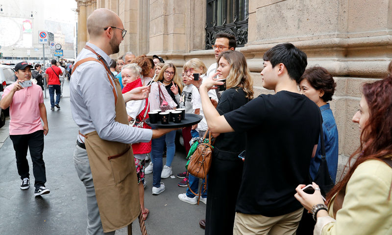 © Reuters. A staff member of Starbucks Reserve Roastery offers coffee to the customers in queue waiting at the entrance, during the opening day in downtown Milan