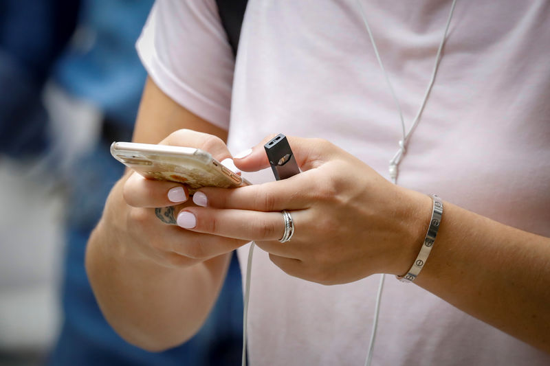 © Reuters. A woman holds a Juul e-cigarette as she uses her phone in New York