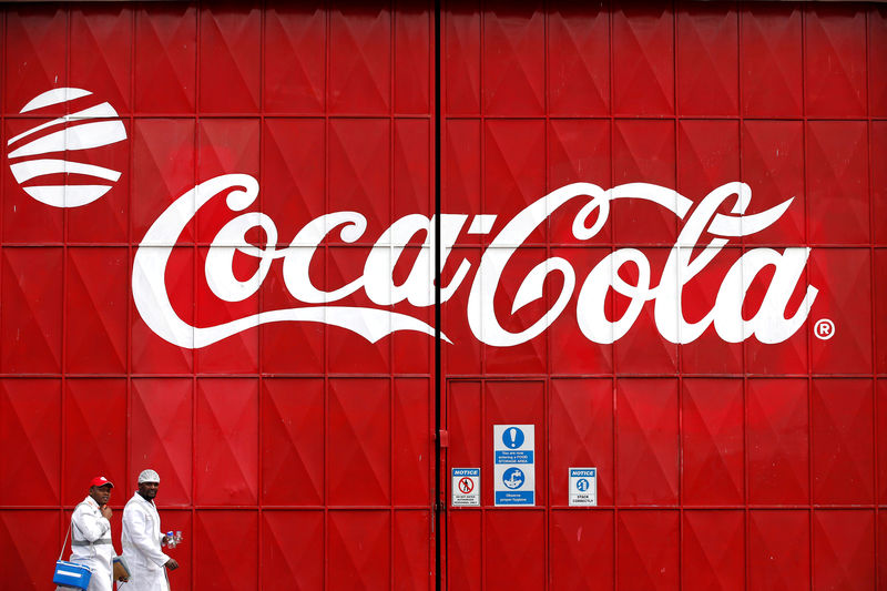 © Reuters. Workers walk past a Coca Cola logo painted on a gate at a Coca Cola factory in Nairobi
