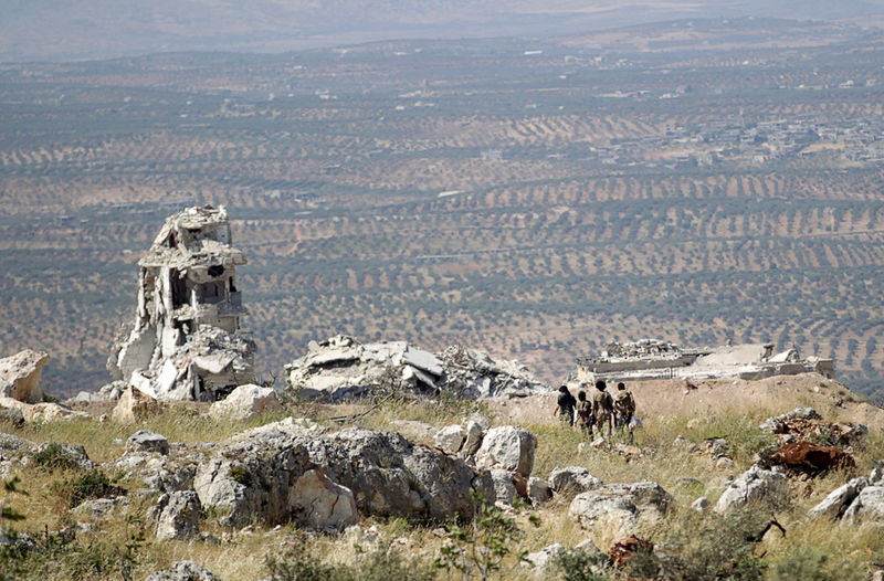 © Reuters. Combatentes rebeldes caminham por montanha com vista para a cidade de Ariha, na província de Idlib, na Síria