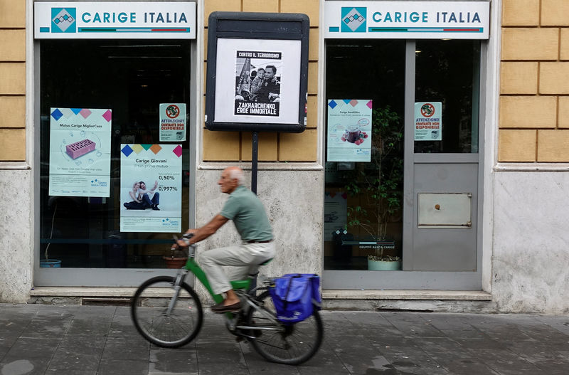 © Reuters. A man rides a bicycle past a Carige bank in Rome