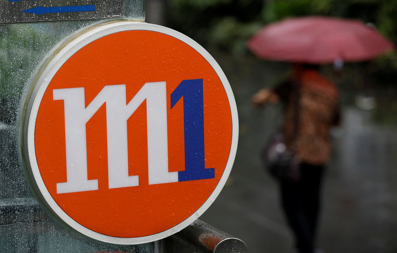 © Reuters. FILE PHOTO: A woman with an umbrella passes an M1 sign in Singapore