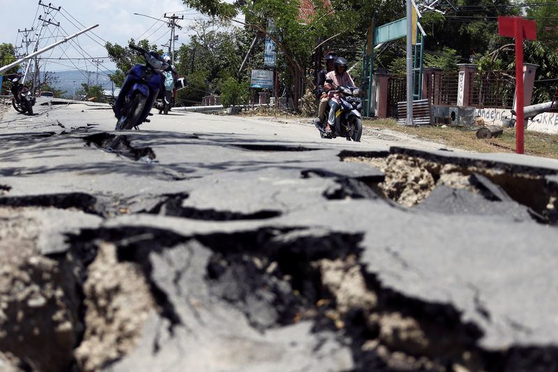 © Reuters. Motorcyclists pass a damaged section of a road following the earthquake in Palu