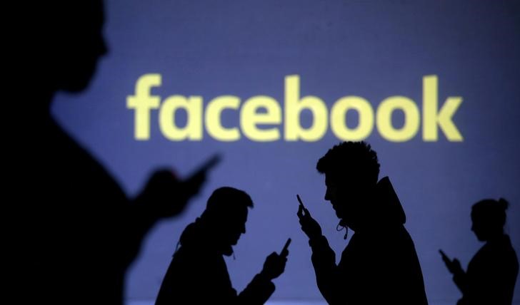 © Reuters. FILE PHOTO: Silhouettes of mobile users are seen next to a screen projection of Facebook logo in this picture illustration