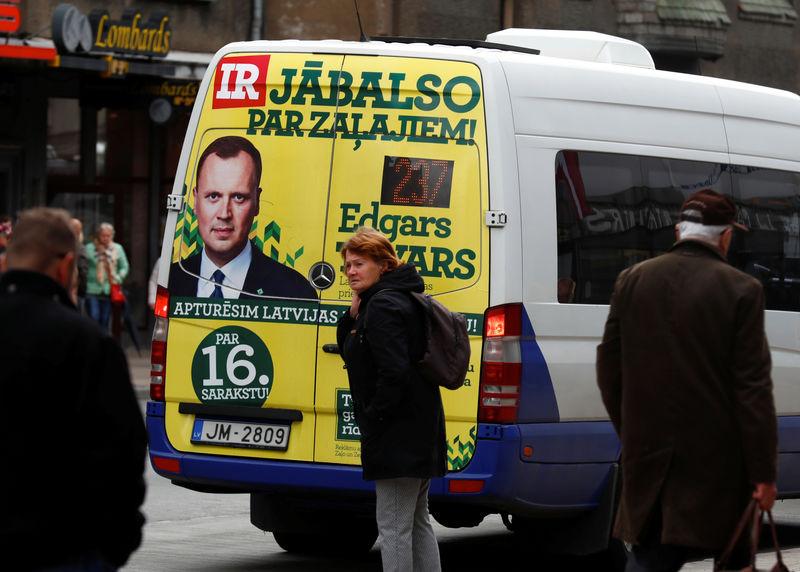 © Reuters. People walk next to a bus with the Union of Greens and Farmers election campaign poster on it in Riga