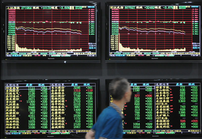 © Reuters. Man walks past screens showing stock information at a brokerage house in Jiujiang