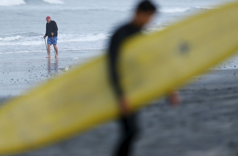 © Reuters. An elderly man exercises along the beach as a surfer carries his surfboard home in La Jolla, California