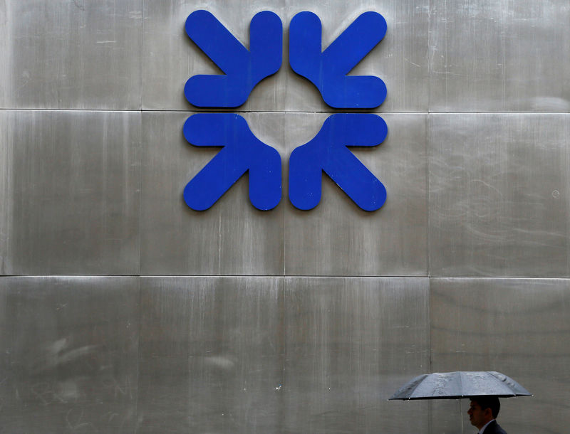 © Reuters. FILE PHOTO: A man shelters under an umbrella as he walks past a branch of the Royal Bank of Scotland London