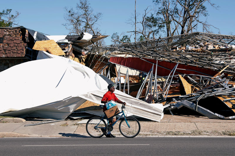 © Reuters. A man carries food and water past a building damaged by Hurricane Michael in Parker