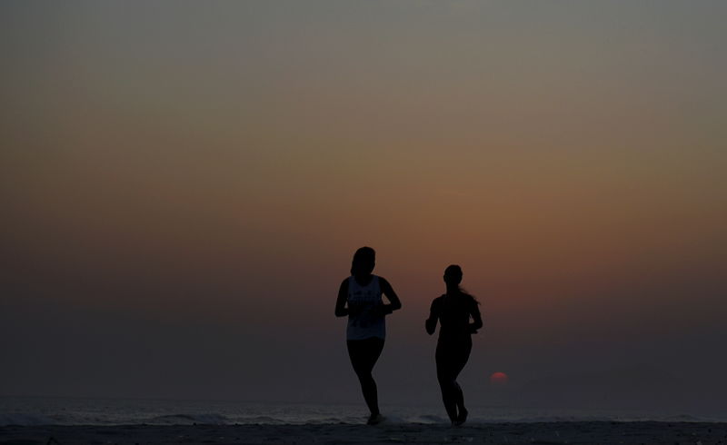 © Reuters. Mulheres correm durante o pôr do sol na praia da Barra da Tijuca, no Rio de Janeiro,