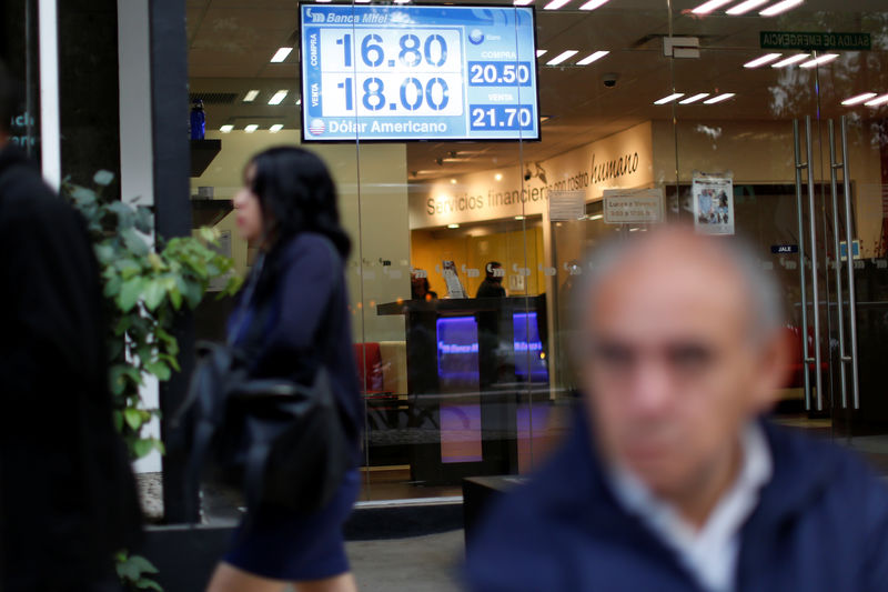 © Reuters. Imagen de archivo de personas caminando mientras se ve una pantalla con la tasa de cambio del peso mexicano contra el dólar en una sucursal del banco Mifel en Ciudad de México