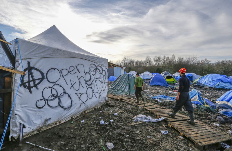 © Reuters. Migrants walk in a muddy field at at a camp of makeshift shelters for migrants and asylum-seekers from Iraq, Kurdistan, Iran and Syria, called the Grande Synthe jungle