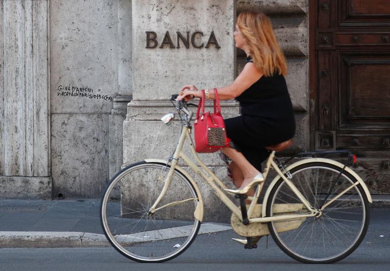 © Reuters. A woman rides a bicycle as she passes in front of a Bank sign in downtown Rome