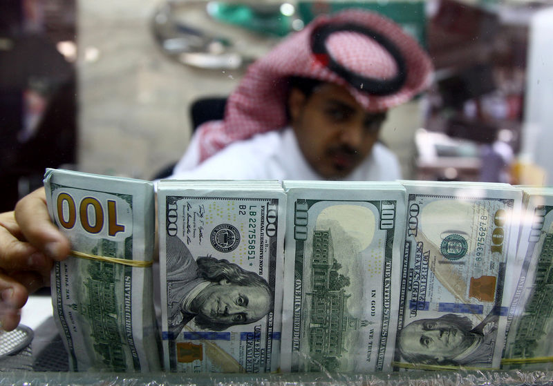 © Reuters. Saudi money changer, pictured through a glass, arranges U.S banknotes at a currency exchange shop in Riyadh