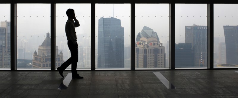 © Reuters. A man talks on a mobile phone as he walks past the view of the Shanghai skyline