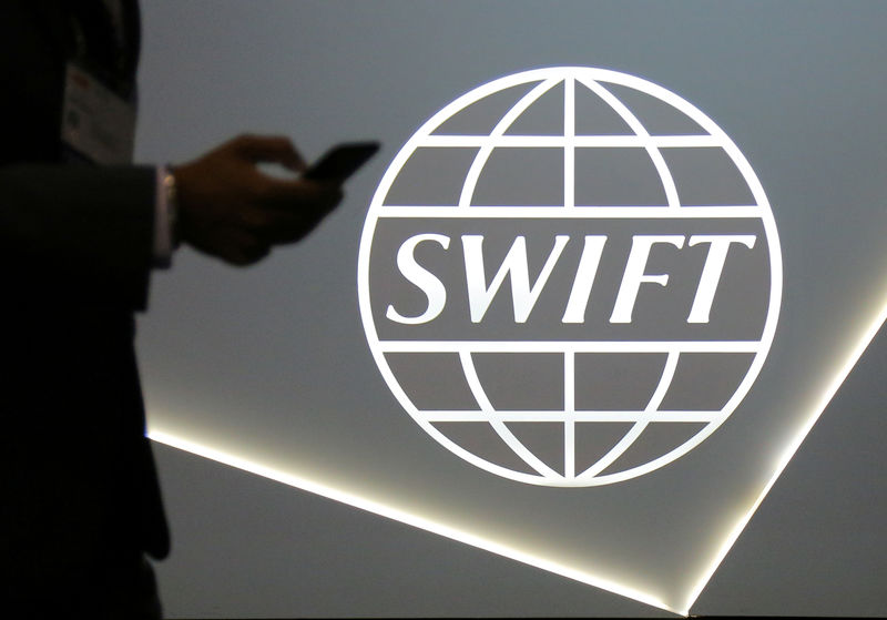 © Reuters. A man using a mobile phone passes the logo of global secure financial messaging services cooperative SWIFT at the SIBOS banking and financial conference in Toronto