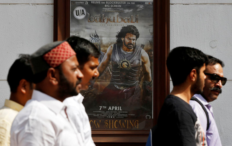 © Reuters. FILE PHOTO: People walk past a poster of an Indian movie "Baahubali: The Beginning" outside a movie theater in New Delhi