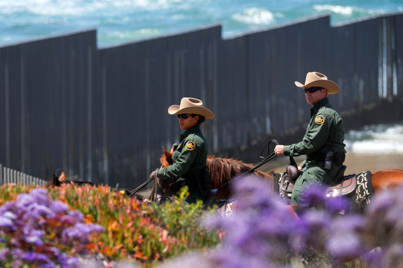 © Reuters. U.S. border patrol agents ride past the U.S.-Mexico border wall on horseback near San Diego
