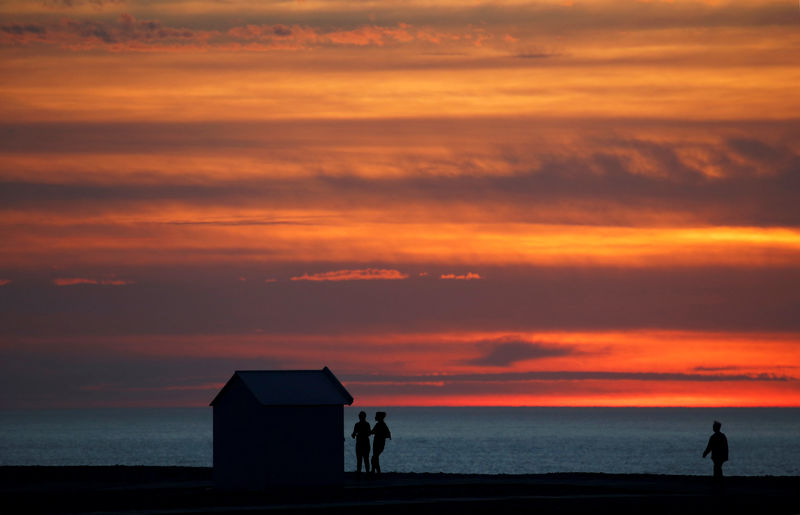 © Reuters. FILE PHOTO: People enjoy a walk at sunset past beach cabin on the pebbled beach in Cayeux-sur-Mer