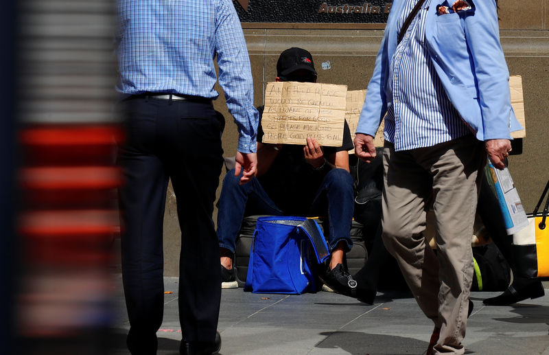 © Reuters. Pedestrians walk past a man holding a sign as he begs for money on a main street in the central business district of Sydney