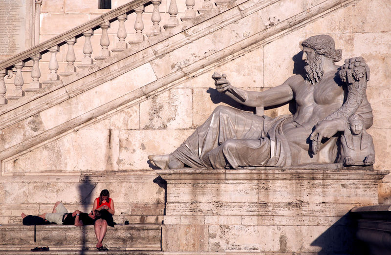 © Reuters. FILE PHOTO: Tourists take a rest near a statue at the top of Capitoline Hill in Rome