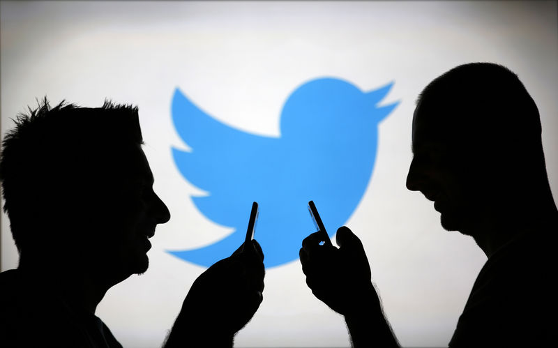 © Reuters. Men are silhouetted against a video screen with a Twitter logo as he poses with a Samsung S4 smartphone in this photo illustration taken in the central Bosnian town of Zenica