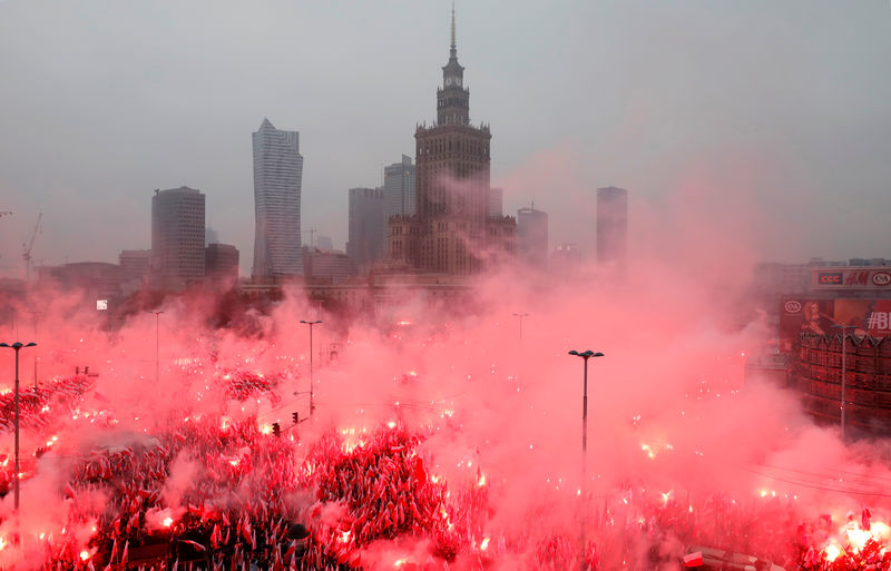 © Reuters. People carry Polish flags and flares as they sing Polish national anthem during a march marking the 100th anniversary of Polish independence in Warsaw