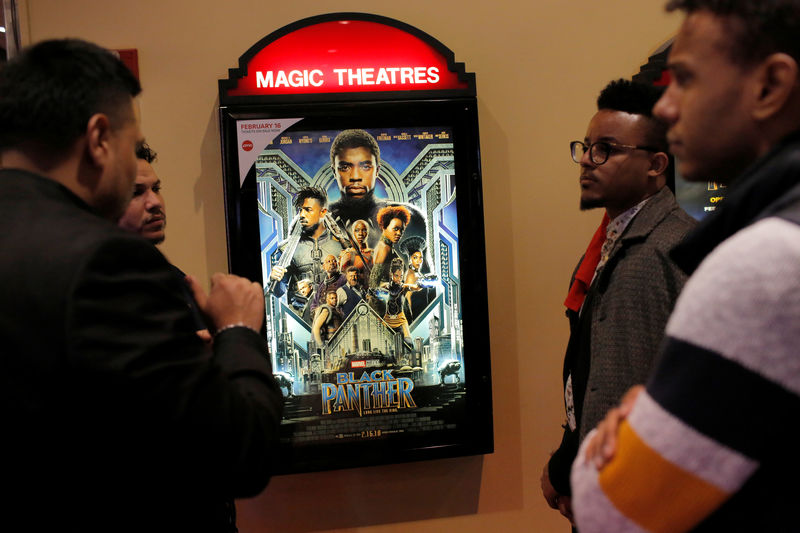 © Reuters. A group of men gather in front of a poster advertising the film "Black Panther" on its opening night of screenings at the AMC Magic Johnson Harlem 9 cinemas in Manhattan