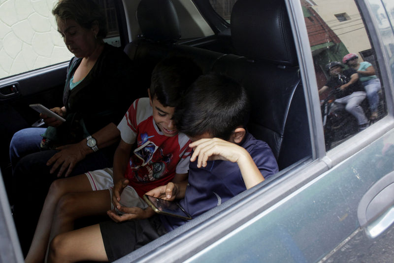 © Reuters. Children play with a cell phone while they wait in a car for gas near a gas station of the Venezuelan state-owned oil company PDVSA in San Cristobal