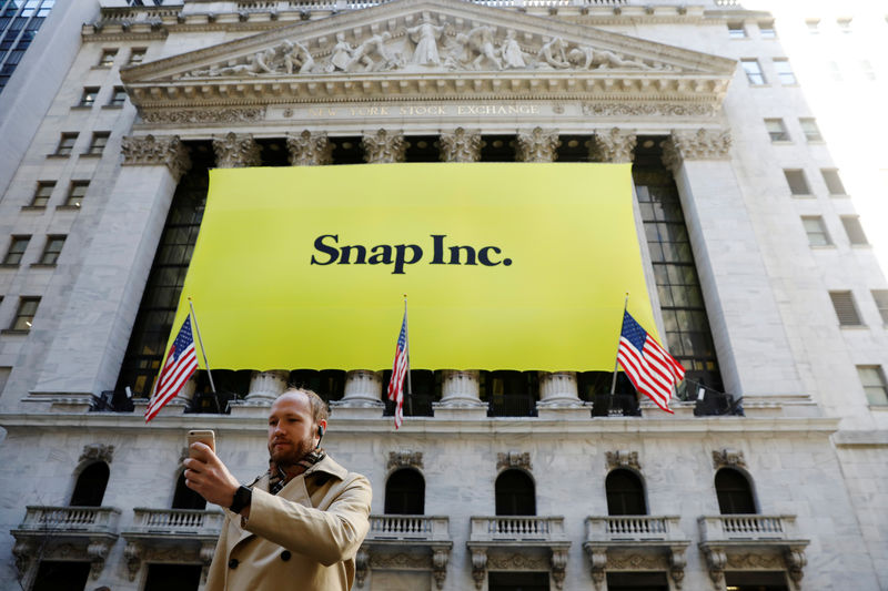 © Reuters. A man takes a photograph of the front of the New York Stock Exchange (NYSE) with a Snap Inc. logo hung on the front of it shortly before the company's IPO in New York