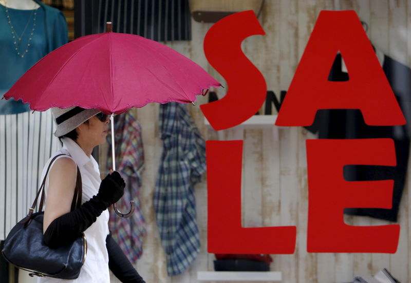 © Reuters. Imagen de archivo de una mujer sosteniendo un paraguas mientras camina frente a una publicidad de ventas afuera de una tienda de una marca de lujo en el distrito comercial de Tokio