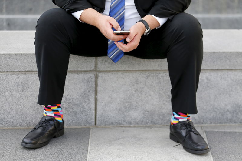 © Reuters. FILE PHOTO - A businessman sits on a bench looking over his mobile phone in downtown San Francisco