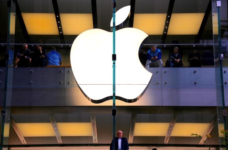 © Reuters. A customer stands underneath an illuminated Apple logo as he looks out the window of the Apple store located in central Sydney