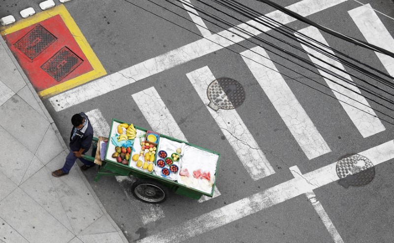 © Reuters. A man pushes a cart loaded with fruit as he sells to customers on a street in Sao Paulo