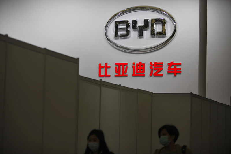 © Reuters. Women walk in front of the logo of Chinese car manufacturer BYD Auto stage before the opening of the 15th Shanghai International Automobile Industry Exhibition