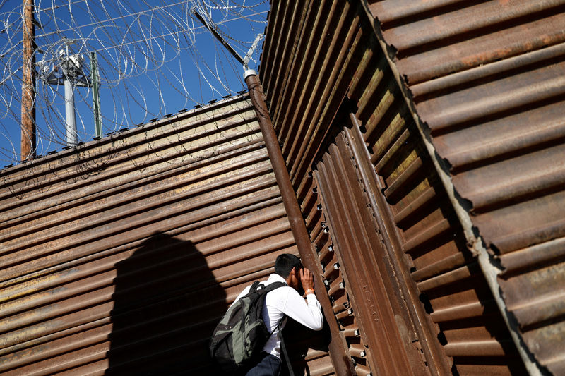 © Reuters. A migrant, part of a caravan of thousands traveling from Central America en route to the United States, looks at U.S. border patrol officers through holes in the border wall between the U.S. and Mexico in Tijuana