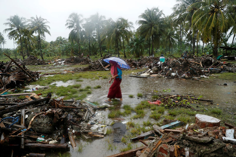 © Reuters. A woman holding an umbrella walks in the rain among debris after a tsunami, in Sumur