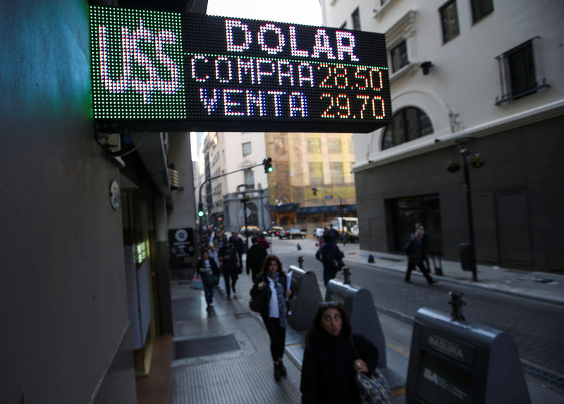 © Reuters. Pedestrians walk past an electronic board showing currency exchange rates in Buenos Aires' financial district