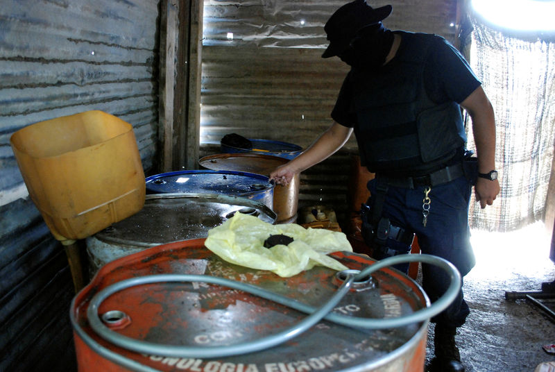 © Reuters. FILE PHOTO: Policeman inspects barrels containing stolen diesel fuel, stored in a tyre repair shop, during an operation in the municipality of Apodaca