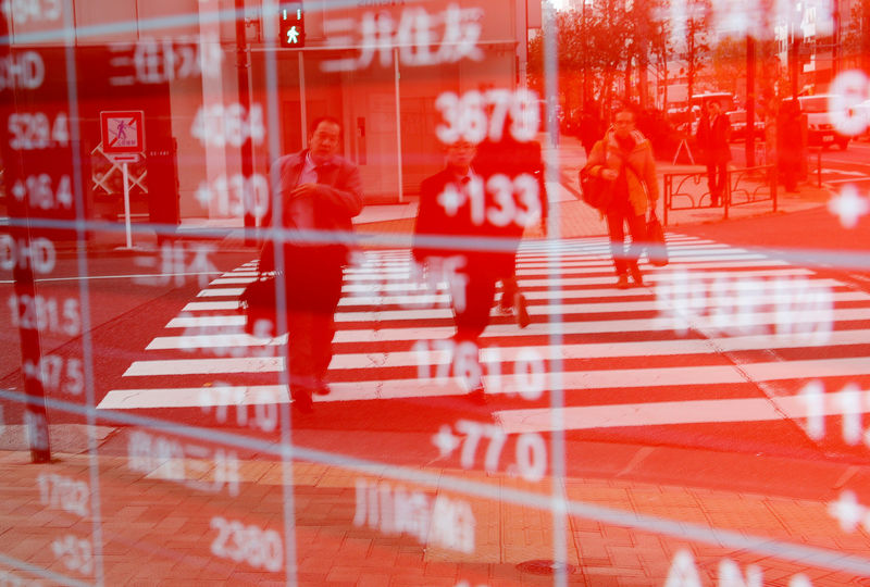 © Reuters. Pedestrians are reflected on an electronic board showing stock prices outside a brokerage in Tokyo