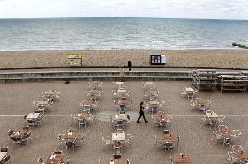 © Reuters. A woman places menu's on tables outside a restaurant on the seafront in Brighton