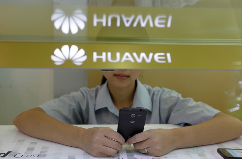 © Reuters. FILE PHOTO: A sales assistant looks at her mobile phone as she waits for customers behind a counter at a Huawei booth in Wuhan