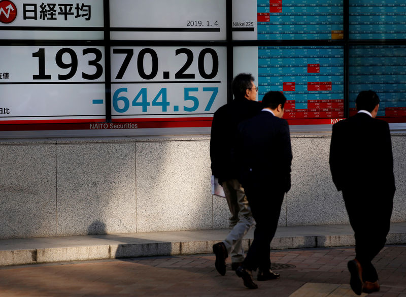 © Reuters. Men walk past an electronic board showing Nikkei average outside a brokerage in Tokyo